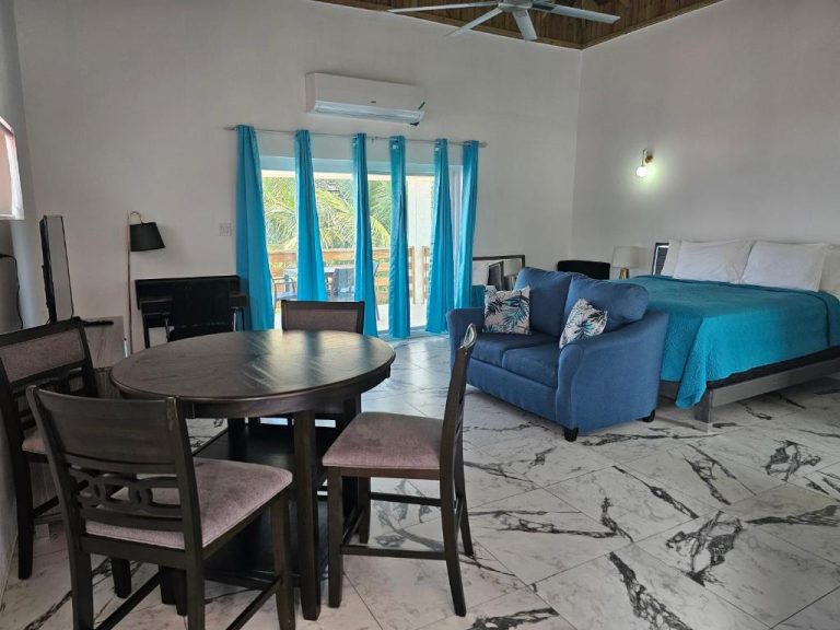 Suite amplia con cama, sofá azul y mesa de comedor en Roots Cafe Negril Rooms con vista a terraza