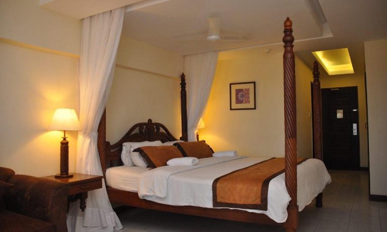 Habitación de lujo con cama de dosel de madera y cortinas blancas en Royal Court Hotel