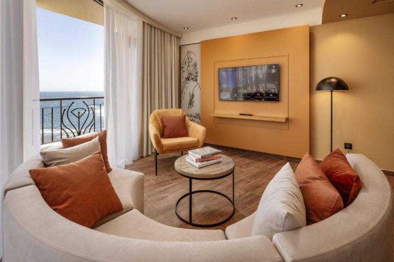 Salón elegante con sofás blancos, TV y balcón con vistas al mar en el Vivaldi Hotel