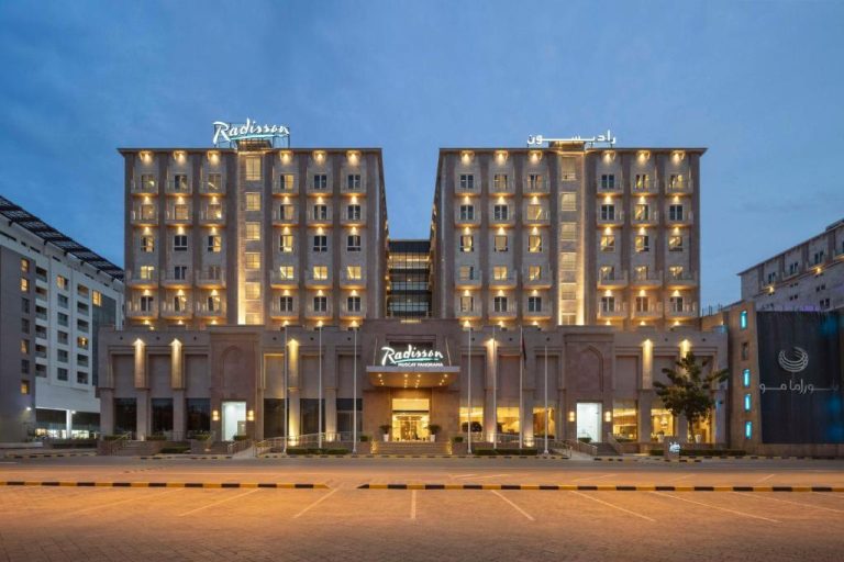 Fachada exterior iluminada del Radisson Hotel Muscat Panorama vista nocturna con dos torres