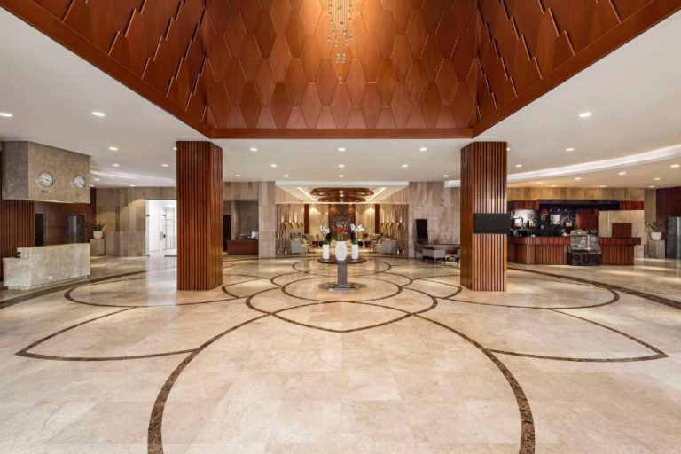 Amplio lobby de mármol con columnas de madera y diseño geométrico en el Radisson Hotel Muscat Panorama