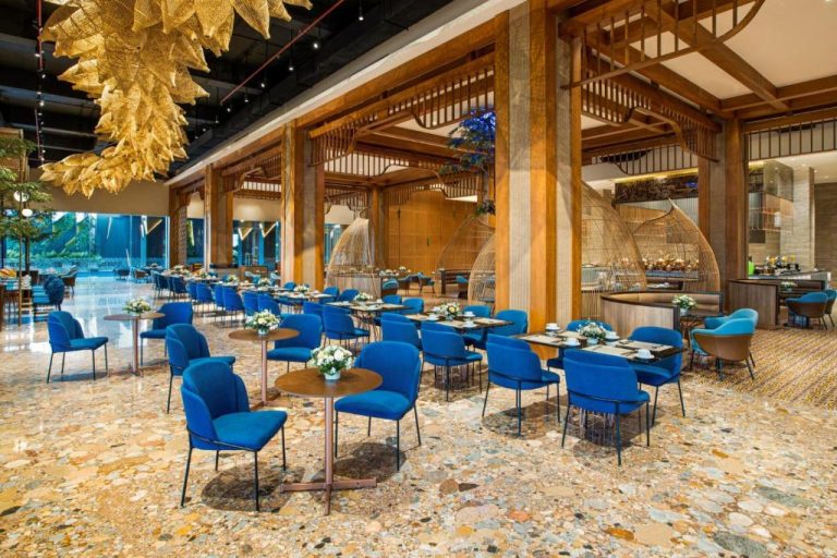 Elegante restaurante del Morazen Yogyakarta con sillas azules, mesas de madera y lámparas doradas decorativas