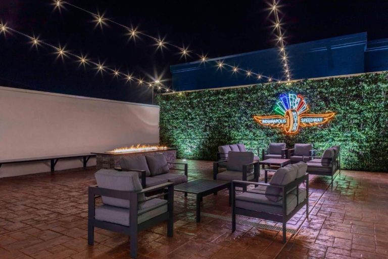 Terraza exterior nocturna con chimenea y letrero neon de Indianapolis Motor Speedway en Hampton Inn West
