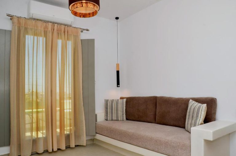 Salón luminoso con sofá marrón y ventana con cortinas en Lilian Studios