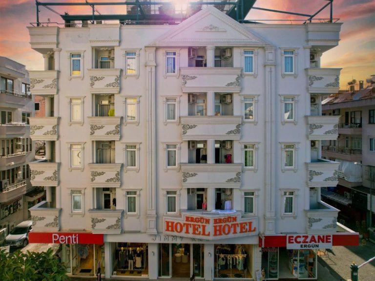 Fachada exterior blanca del Ergün Otel con decoración clásica y tiendas en planta baja al atardecer