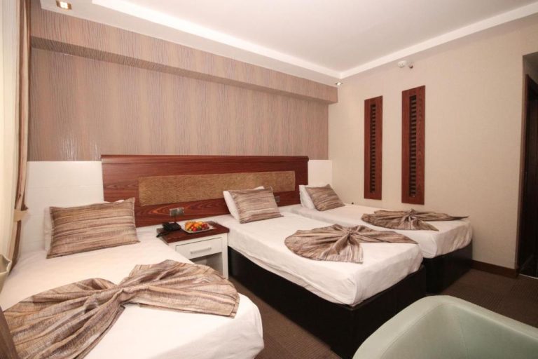 Habitación triple con tres camas individuales y decoración elegante en madera del Mostar Hotel Antalya