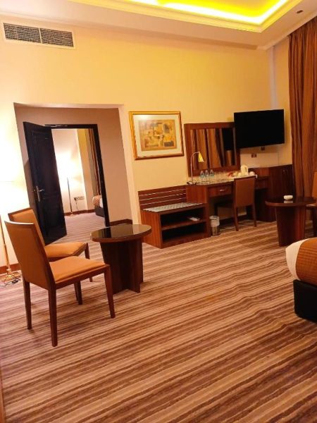 Amplia suite con salón, escritorio y televisión del Royal Qatar Hotel con elegante decoración en tonos cálidos