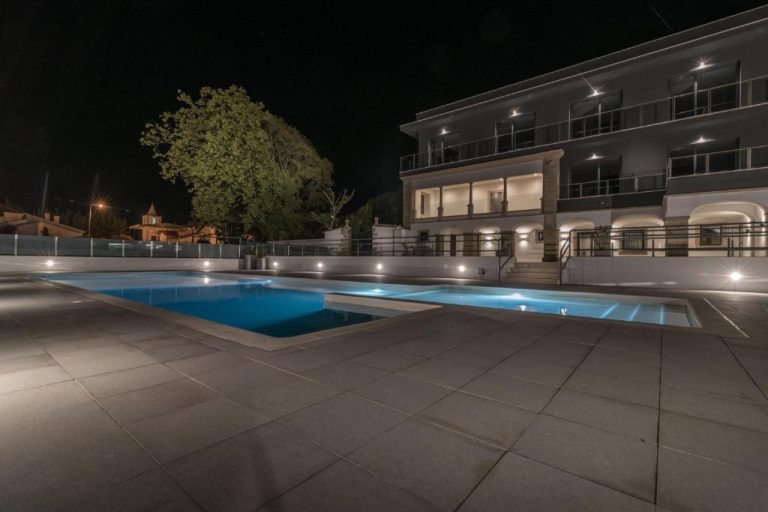 Piscina exterior iluminada de noche en Casa do Adro Hotel de Charme con vistas a la fachada del hotel