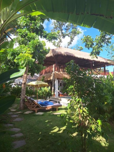 Bungalow con techo de paja y jardín tropical con tumbonas en el Hotel Twiny's