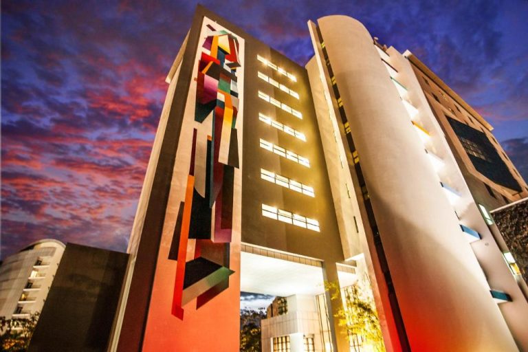 Fachada exterior del Hennessy Park Hotel de noche con mural colorido y arquitectura moderna iluminada