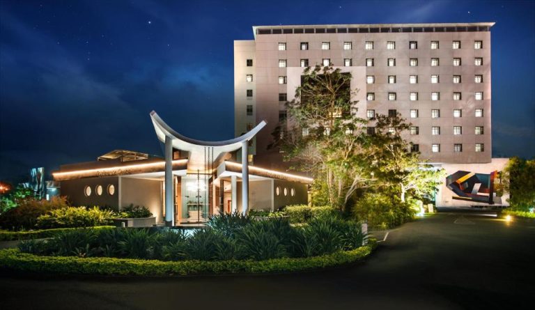 Fachada exterior iluminada del Hennessy Park Hotel con jardines tropicales y entrada principal de noche