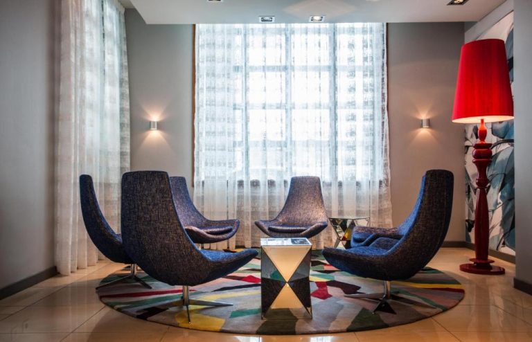 Sala de espera moderna con sillones azules y alfombra colorida en el lobby del Hennessy Park Hotel