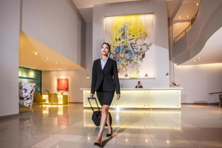 Mujer de negocios con maleta en el moderno lobby del Hennessy Park Hotel con recepción iluminada