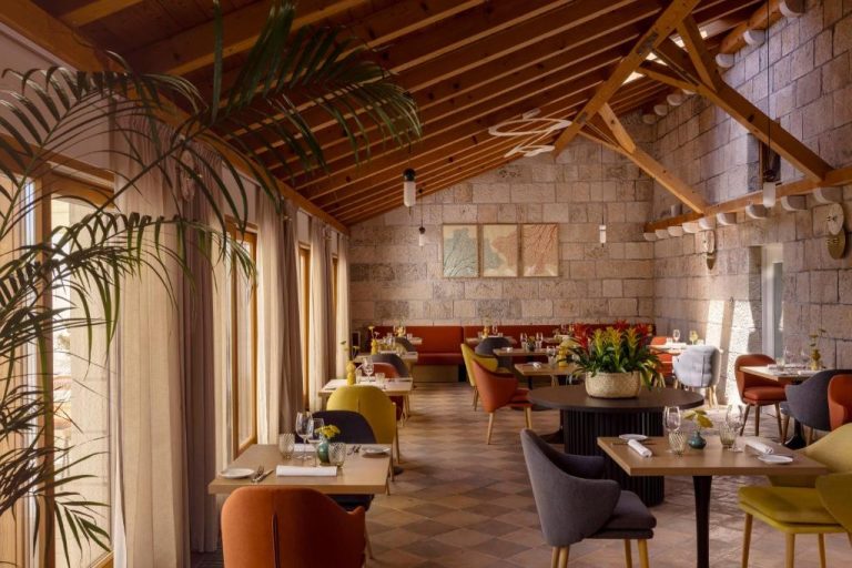 Restaurante interior del Palace Natali con sillas coloridas, techumbre de madera y paredes de piedra natural