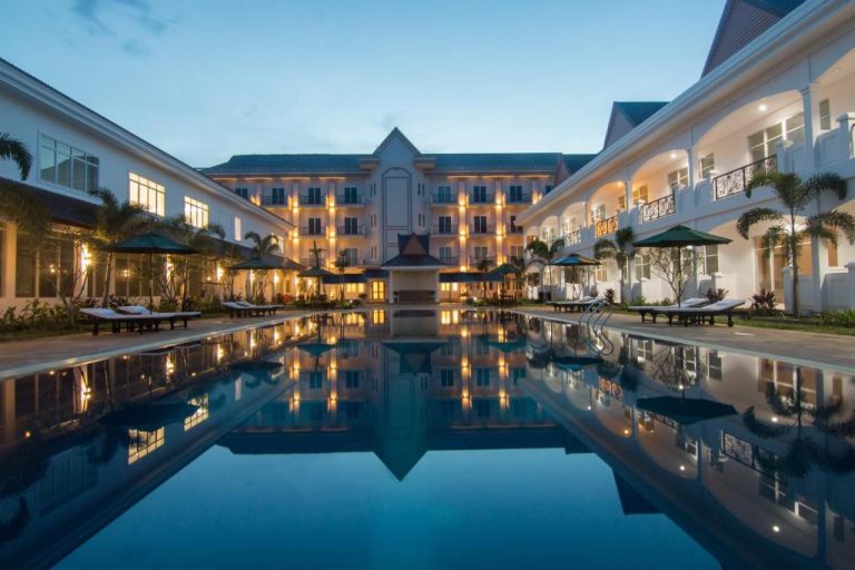 Piscina exterior iluminada del Glorious Hotel al atardecer con tumbonas y palmeras tropicales