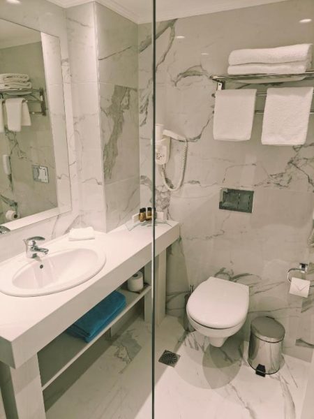 Baño moderno con mármol blanco, ducha acristalada y lavabo del Ibiscus Hotel