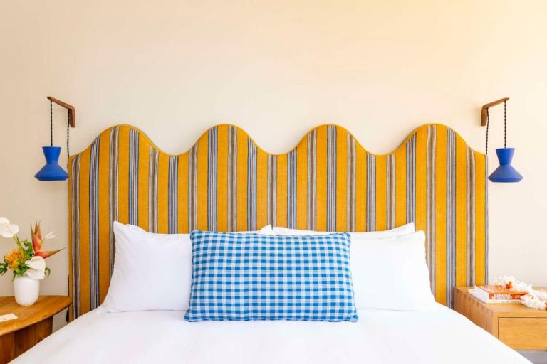 Habitación con cabecero ondulado amarillo a rayas y cojín azul en Wayfinder Waikiki Hawaii