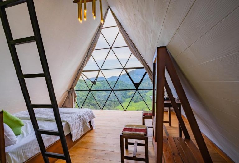 Habitación domo geodésico con cama y ventana triangular con vistas a montañas verdes en Eco Vibe Resort