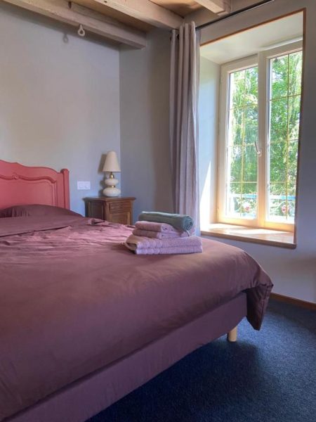 Habitación doble con cabecero rosa y ventana con vistas al jardín en Moulin de Petoulle