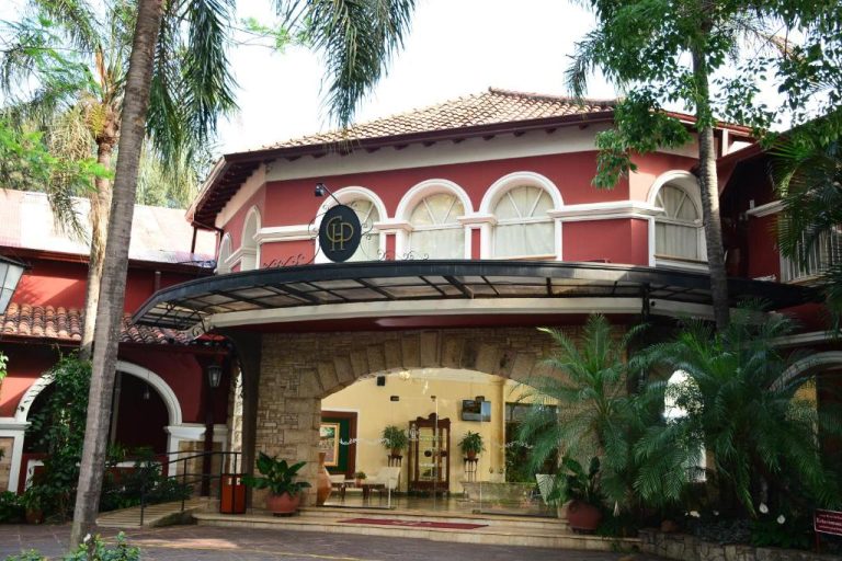 Entrada principal del Gran Hotel del Paraguay con fachada colonial roja y jardines tropicales
