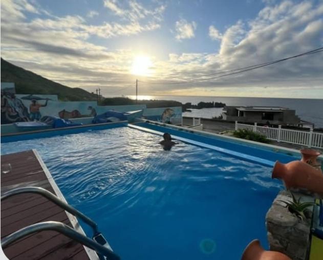 Piscina infinita con vistas al océano al atardecer en Fajã Beach House con murales decorativos