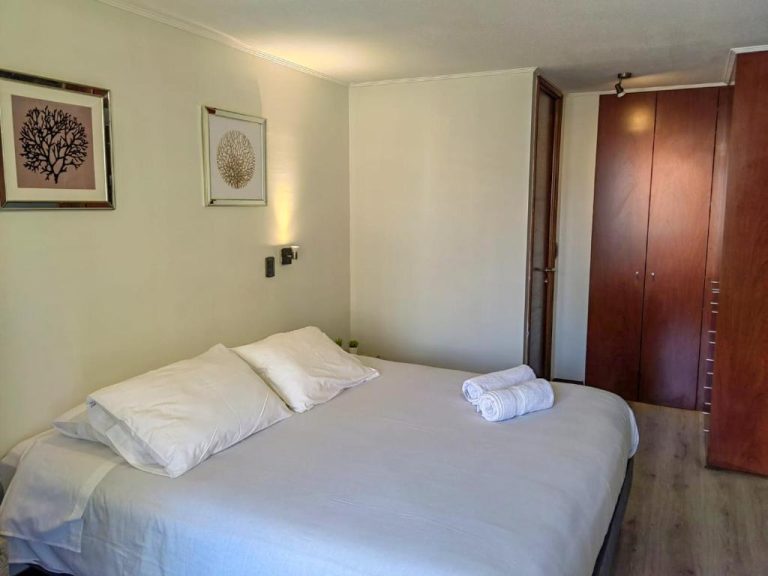 Habitación doble con cama matrimonial y armario de madera en Apart Barrio El Golf con piscina