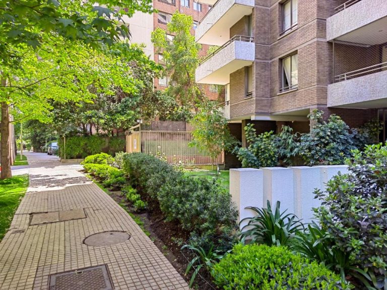 Jardín exterior con arbustos y árboles frondosos en Apart Barrio El Golf con piscina en Santiago