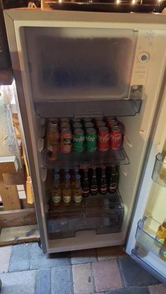 Nevera con bebidas y refrescos disponibles en La Felicidad Aruba, incluyendo Coca-Cola y Sprite
