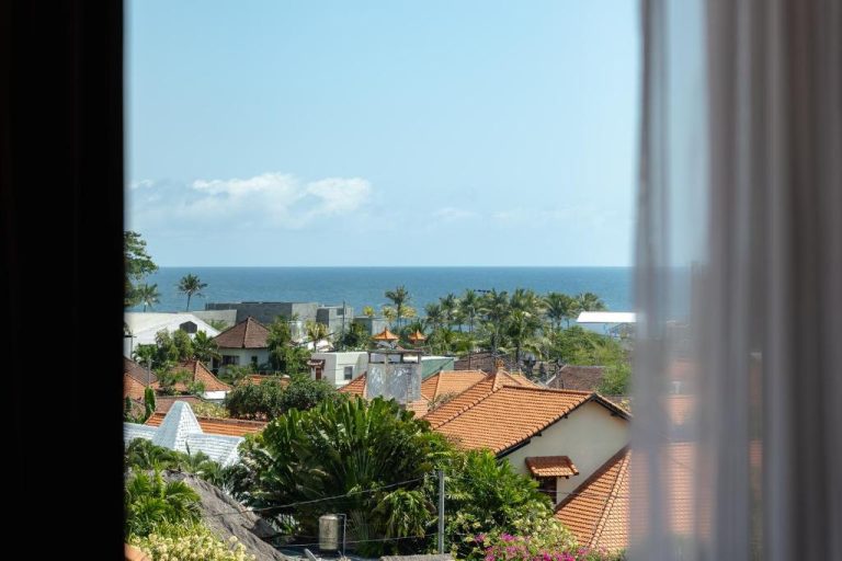 Vista panorámica al mar desde ventana del Sunny Aparts 2 con tejados y palmeras tropicales