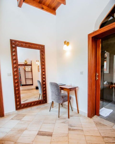 Habitación con escritorio de madera, espejo de pie y acceso al baño en The Seyyida Hotel and Spa