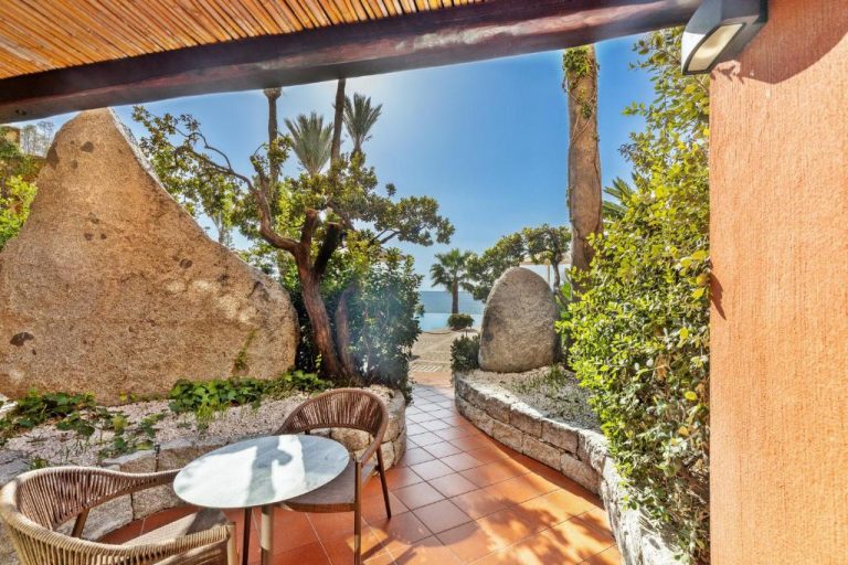Terraza con mesa y sillas rodeada de rocas y jardín con vistas al mar en Hotel La Bitta Bovis Hotels