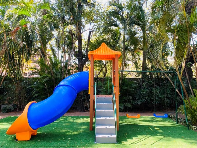 Área de juegos infantil con tobogán azul y columpios del Gran Hotel del Paraguay rodeada de palmeras