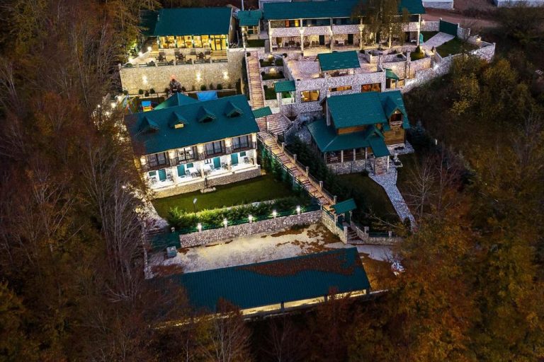 Vista aérea nocturna del Garni Hotel Elite Resort con tejados verdes y jardines iluminados entre bosque