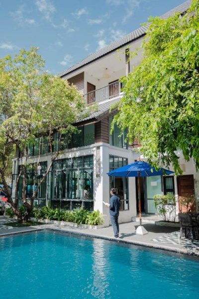 Piscina exterior con sombrilla azul y jardín tropical del Paraiso Hotel Chiangmai en Tailandia