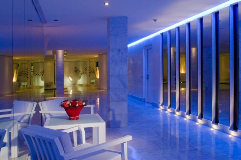 Elegante lobby del Cesar Resort & Spa con iluminación azul LED y mobiliario blanco con flores rojas