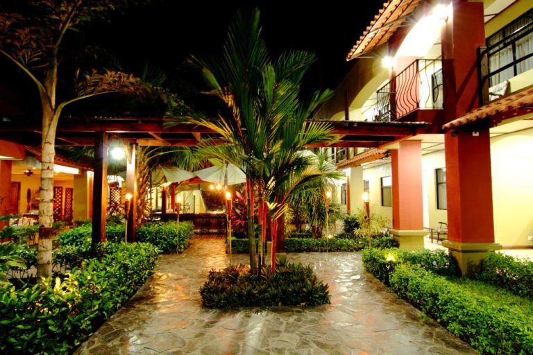 Jardín tropical iluminado de noche con palmeras y camino de piedra en Hotel Boutique Iguana Verde