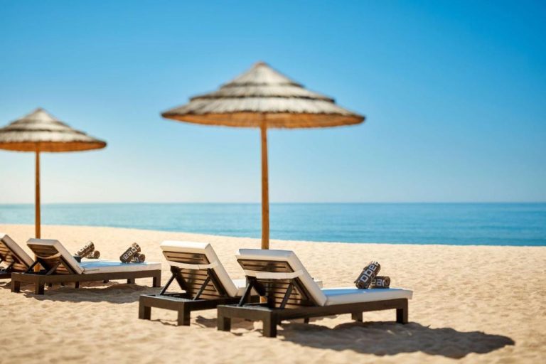 Tumbonas con sombrillas de paja en la playa privada del Tivoli Marina Vilamoura con vistas al mar