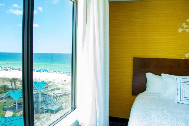 Habitación con cama doble y gran ventanal con vistas al mar y playa en Wavecrest Lodge