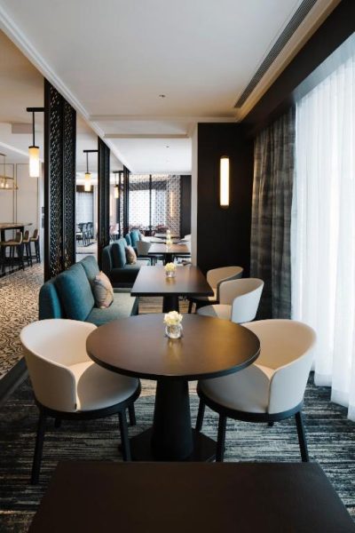 Elegante salón lounge del Grand Park City Hall con mesas redondas y sillones modernos en tonos blancos y azules
