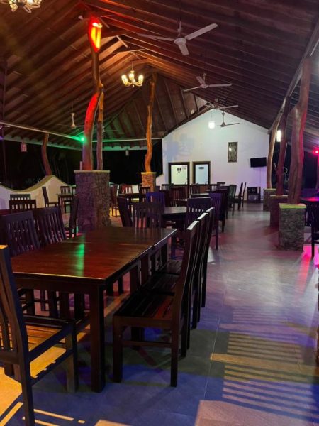 Restaurante interior del Royal Green Garden Puttalam con mesas de madera y ambiente nocturno tropical