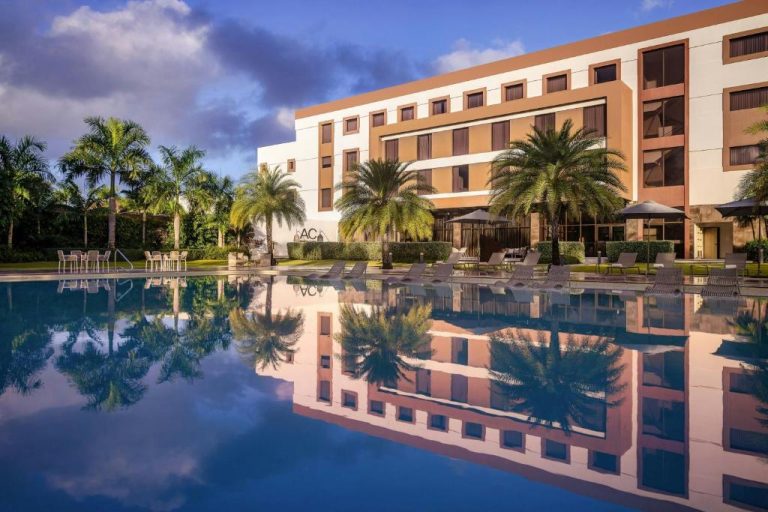 Piscina exterior con reflejo del edificio y palmeras en el AC Hotel by Marriott Punta Cana