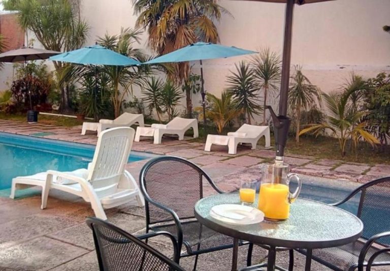 Área de piscina exterior con camastros y sombrillas azules en Íkaro Suites Cancún