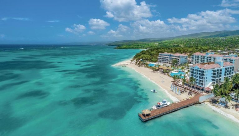 Vista aérea del Sandals Dunns River con playa de arena blanca, muelle privado y aguas turquesas del Caribe