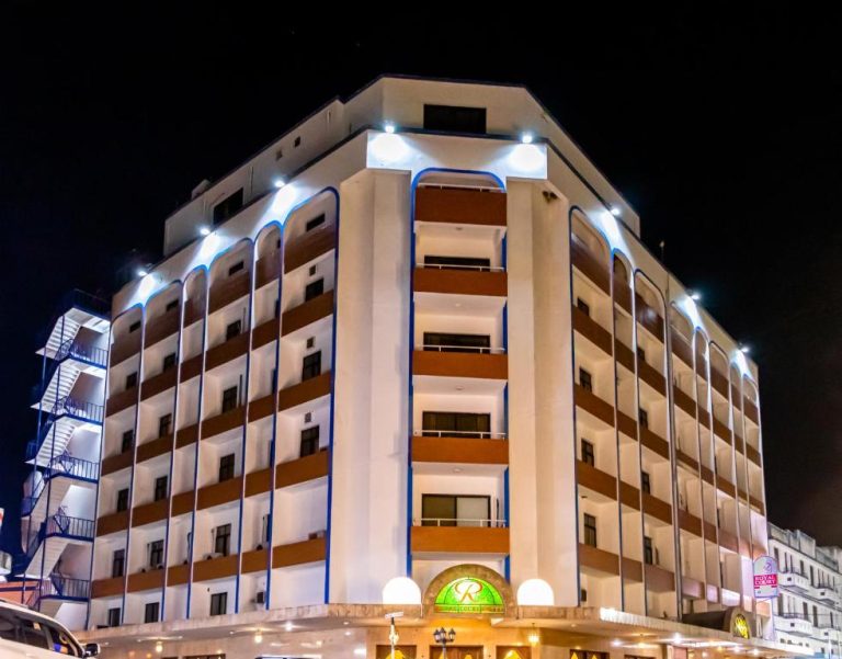 Fachada exterior iluminada del Royal Court Hotel durante la noche con arquitectura moderna