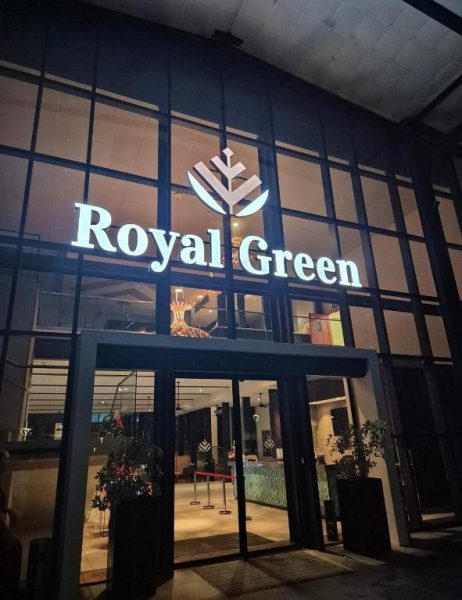 Entrada principal iluminada del Royal Green Wellness Resort durante la noche con fachada de cristal
