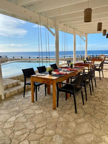 Terraza restaurante con mesas de madera y piscina infinita frente al mar en Begona Cliff Hotel