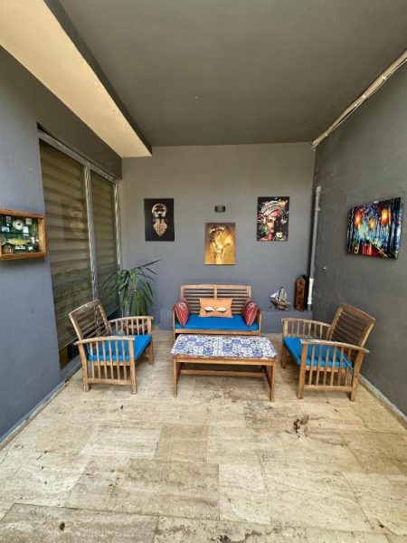 Terraza exterior con sillones de madera y cojines azules en Hotel Alanya Afd, decorada con cuadros artísticos