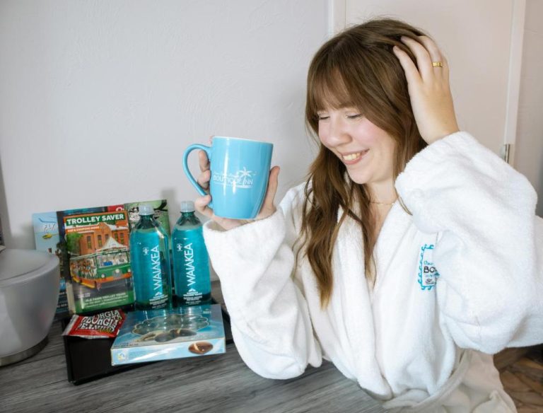 Huésped en bata blanca disfrutando taza de café y amenidades de bienvenida en Ocean Sands Beach Boutique Inn