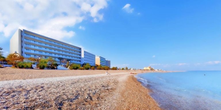 Vista de la playa de arena y guijarros frente al Mediterranean Hotel con su imponente fachada blanca