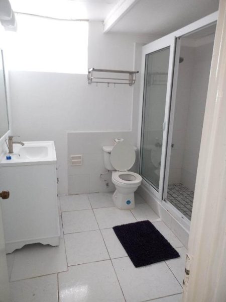 Baño privado con ducha de cristal, lavabo y suelo de baldosas blancas en Negril Beach Club Condos